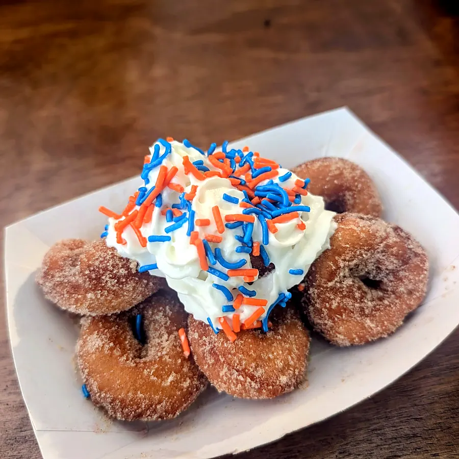 Mini cinnamon sugar donuts in a paper boat topped with whipped cream and sprinkles
