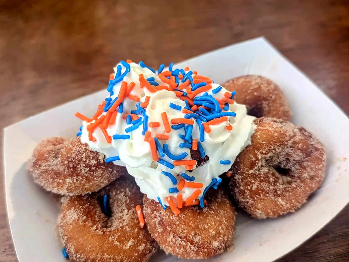 Mini cinnamon sugar donuts in a paper boat topped with whipped cream and sprinkles