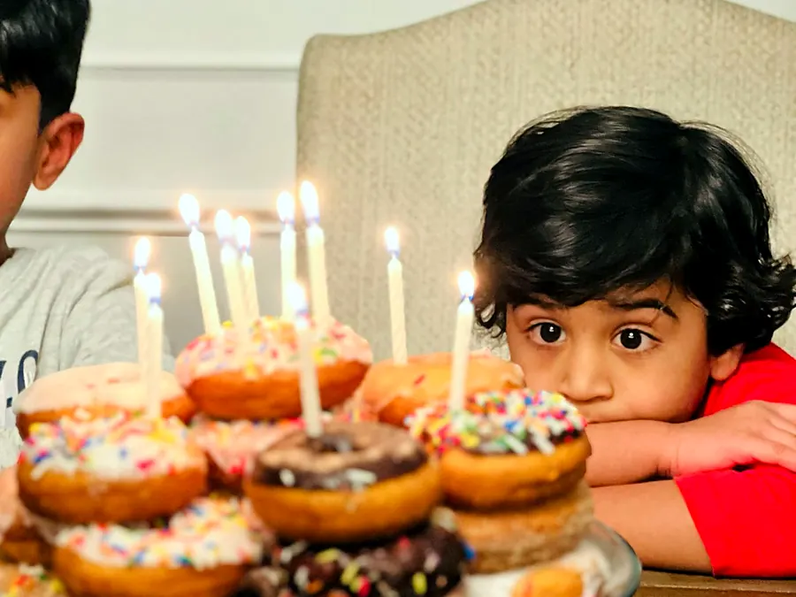 Birthday party: a boy blowing out candles on a tower of donuts with sprinkles
