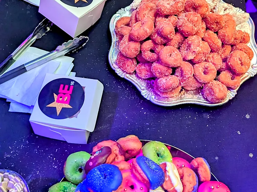 Colorful rainbow mini donuts piled on platters beside branded donut boxes