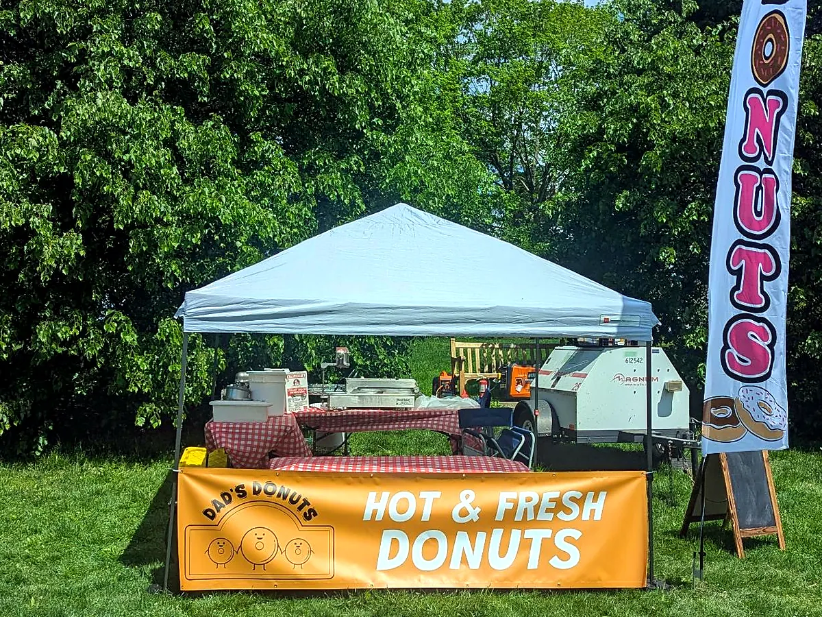 Dad's Donuts tent with a Hot and Fresh Donuts banner and flag set up on a lawn